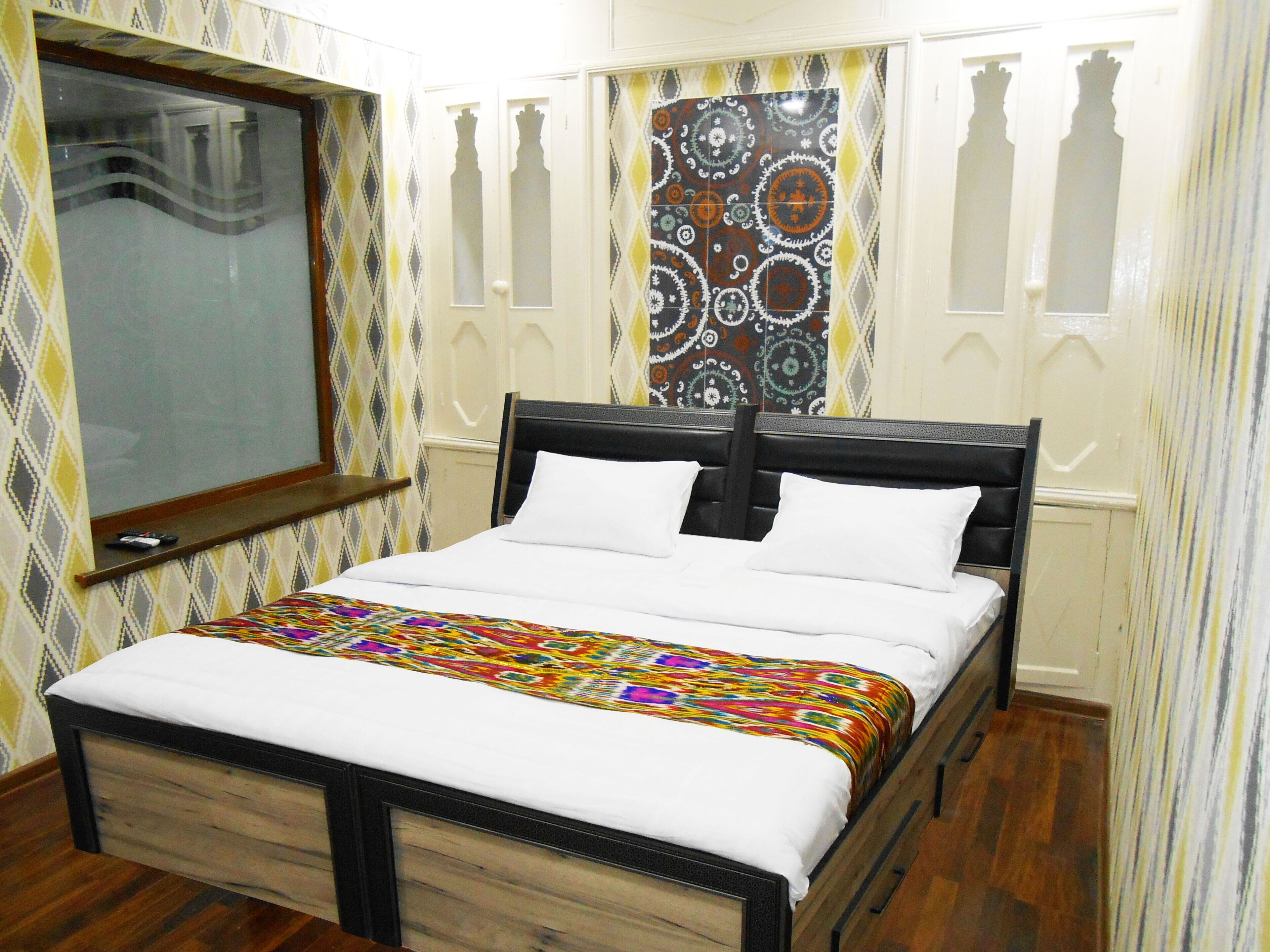 A bedroom with a bed, a window, patterned wallpaper, and wooden flooring.