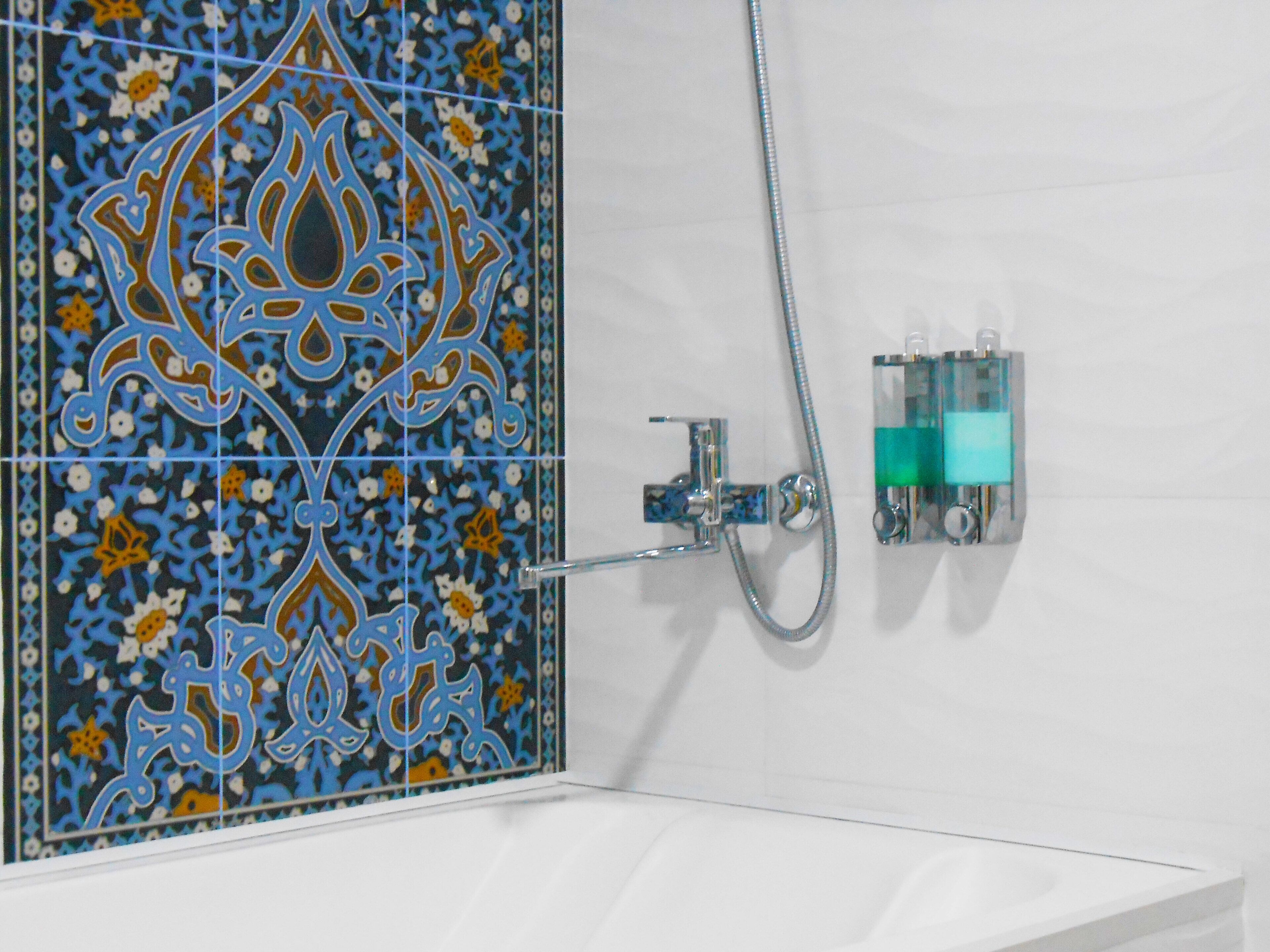 Un baño con un lavamanos blanco, una ducha con manguera cromada y una pared con diseño de azulejos azules y blancos.
