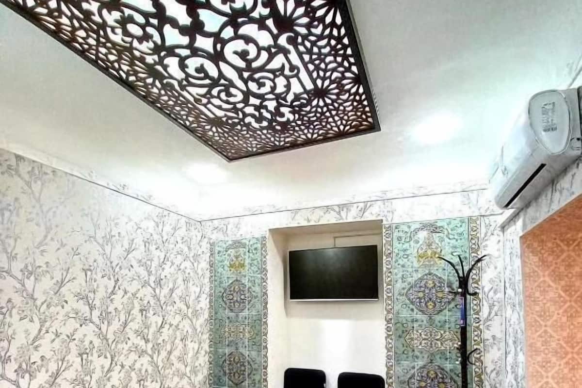Une pièce avec un plancher en bois, un bureau, deux chaises, un téléviseur fixé au mur et un papier peint à motifs.