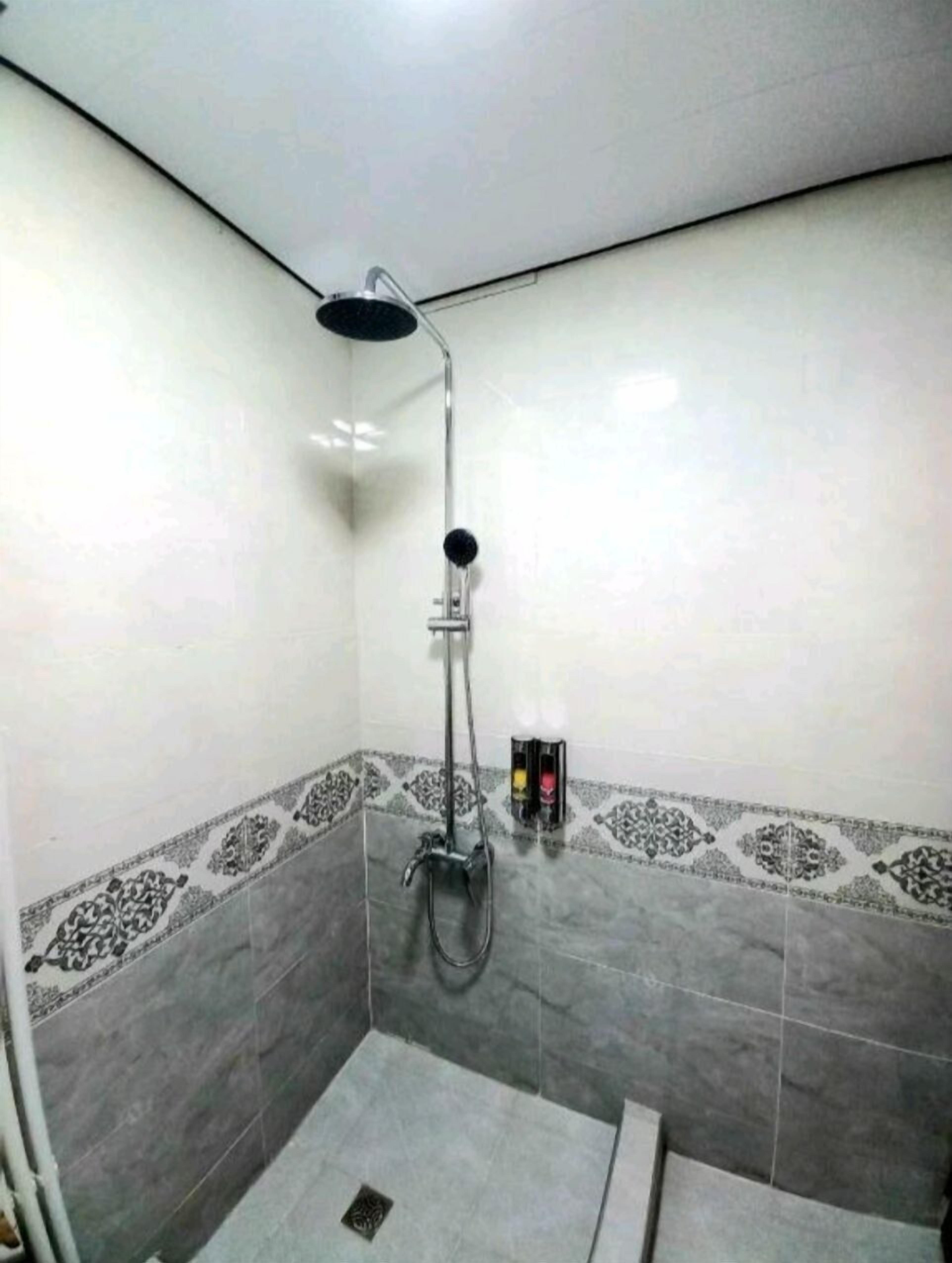 A small, tiled shower area with a handheld showerhead and a wall-mounted control panel.