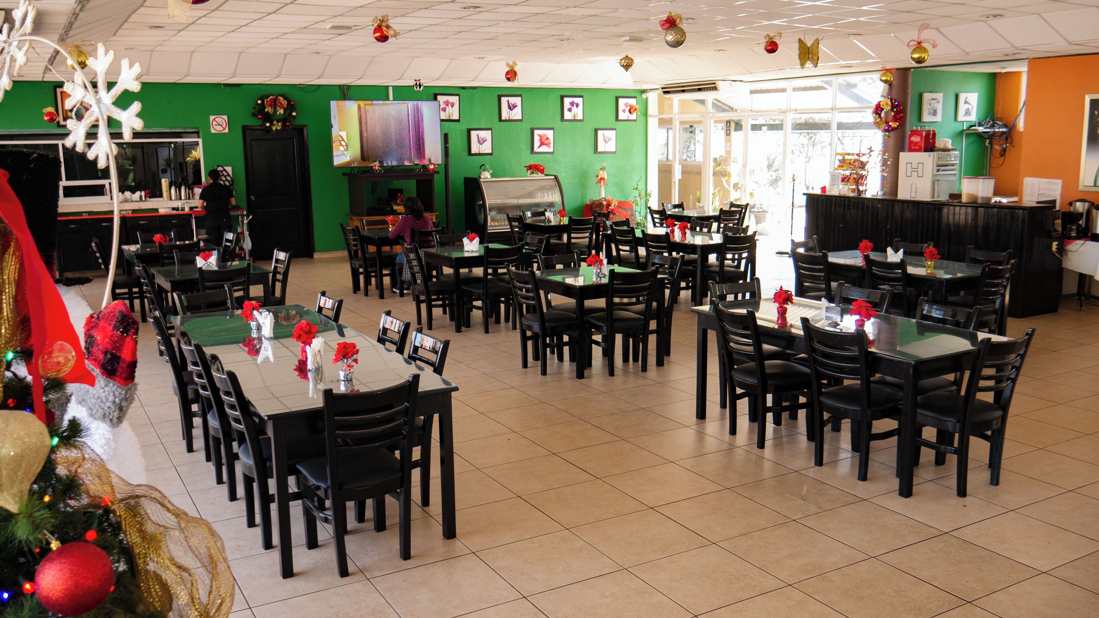 A dining area with multiple tables and chairs, green walls, and Christmas decorations.