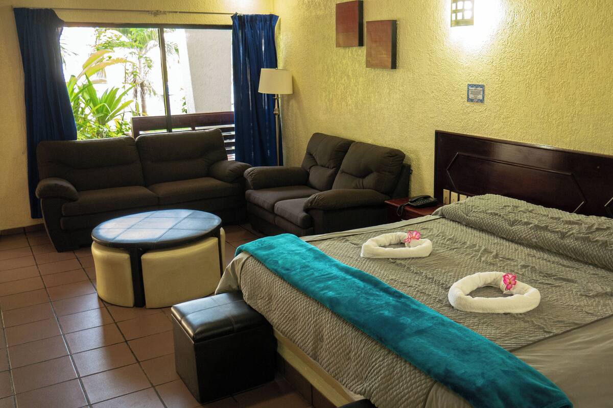 A hotel room with a bed, a sofa, a chair, and a small table.