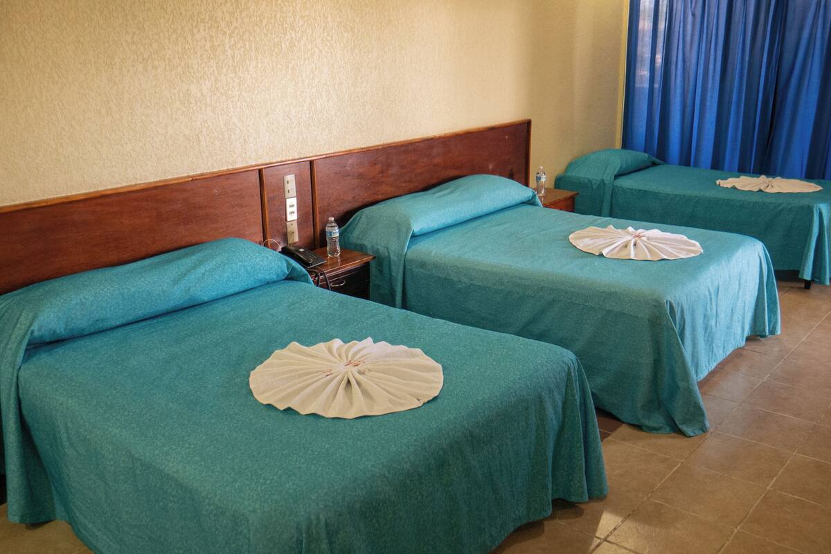 A hotel room with three beds, each with a teal bedspread and a decorative fan.