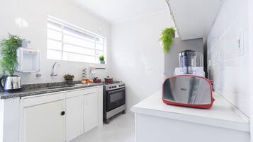 Cozinha moderna com armários brancos, fogão a gás, pia e liquidificador vermelho na bancada.