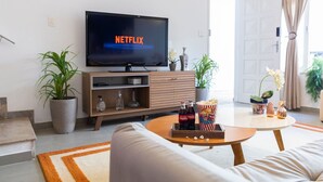 A modern living room with a flat-screen TV displaying 'NETFLIX', a wooden coffee table with snacks, a sofa, and potted plants. - Casa com 4 quartos na Vila Madalena (São Paulo)