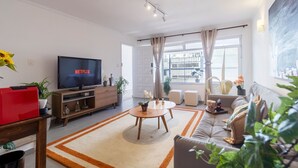 A modern living room with a flat-screen TV, a sofa, a coffee table, and a large window with curtains. - Casa com 4 quartos na Vila Madalena (São Paulo)