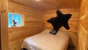 Een houten kamer met een bed, een stervormig kussen, een raam en een plafondlamp.