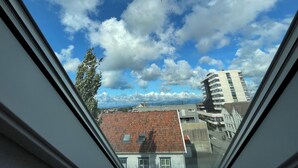A view through a window of a building with a tiled roof, a tree, and a multi-story structure in the background. - Stunning Hilltop Nest Unparalleled Views at BnB Ap 17 (Stavanger)