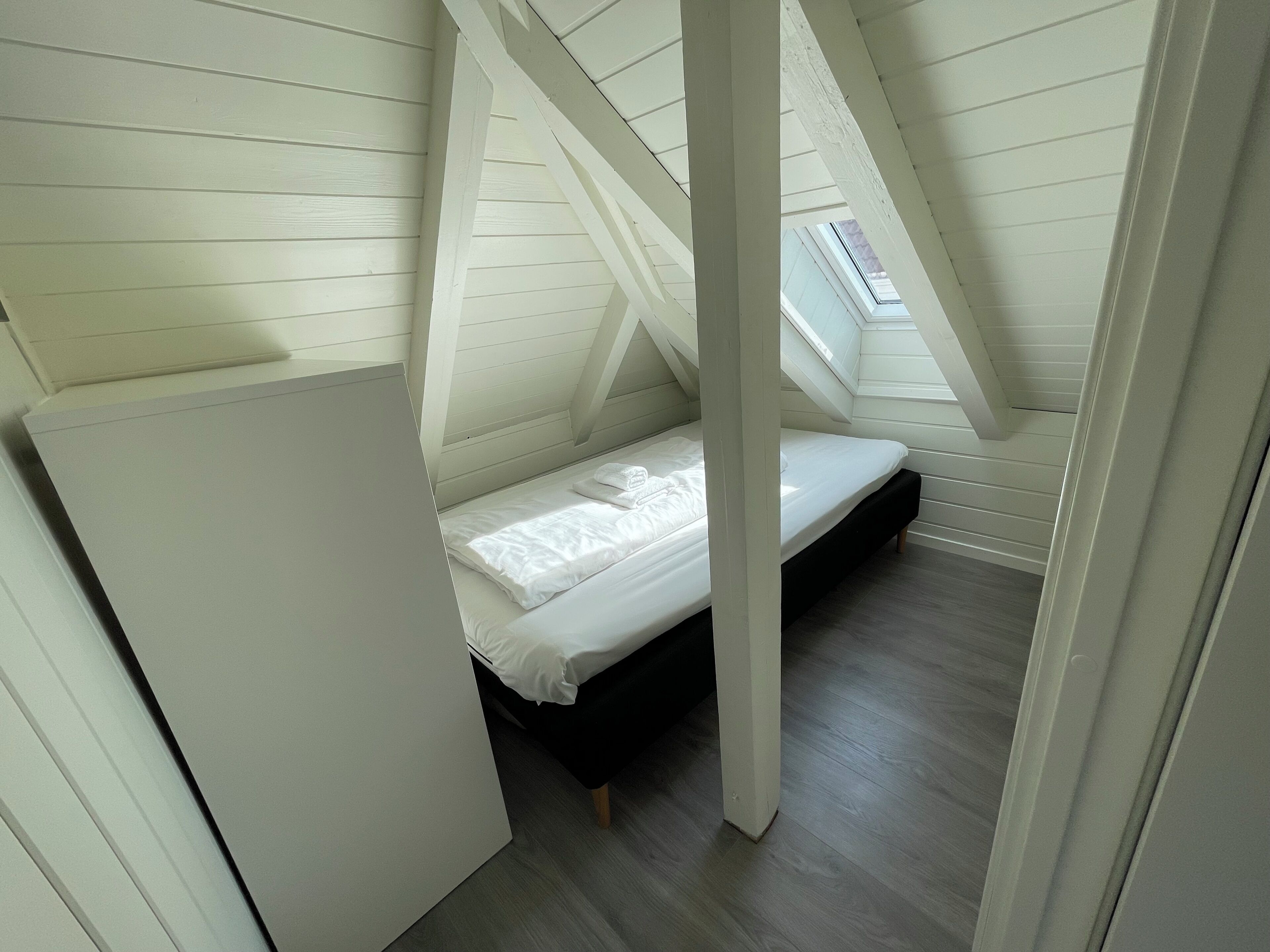 A small, sloped ceiling room with a single bed, wooden beams, and a skylight.