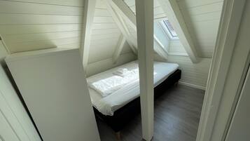 A small, sloped ceiling room with a single bed, wooden beams, and a skylight.