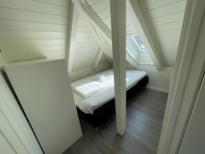 Une petite pièce avec un plafond en pente, un lit simple, des poutres en bois et un puits de lumière.