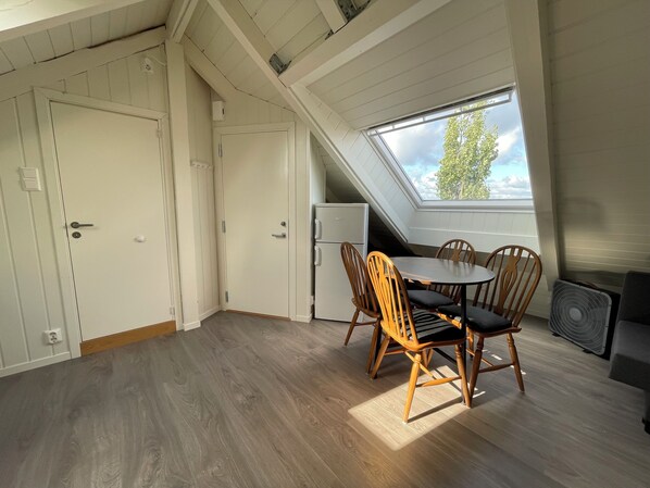Une pièce dotée d’une lucarne, d’une table à manger avec des chaises, d’un petit réfrigérateur et d’un ventilateur.