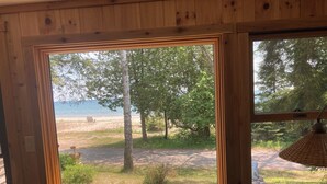 Une cabane en bois dotée d’une grande fenêtre donnant sur une plage et une forêt.