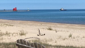 Une plage avec un banc en bois, un phare rouge et un navire à l’horizon.