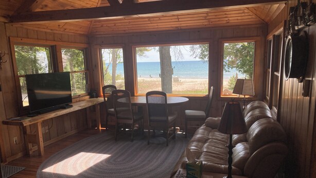 Une cabane en bois équipée d’une télévision, d’une table à manger, de chaises et d’un canapé. De grandes fenêtres offrent une vue sur la plage.