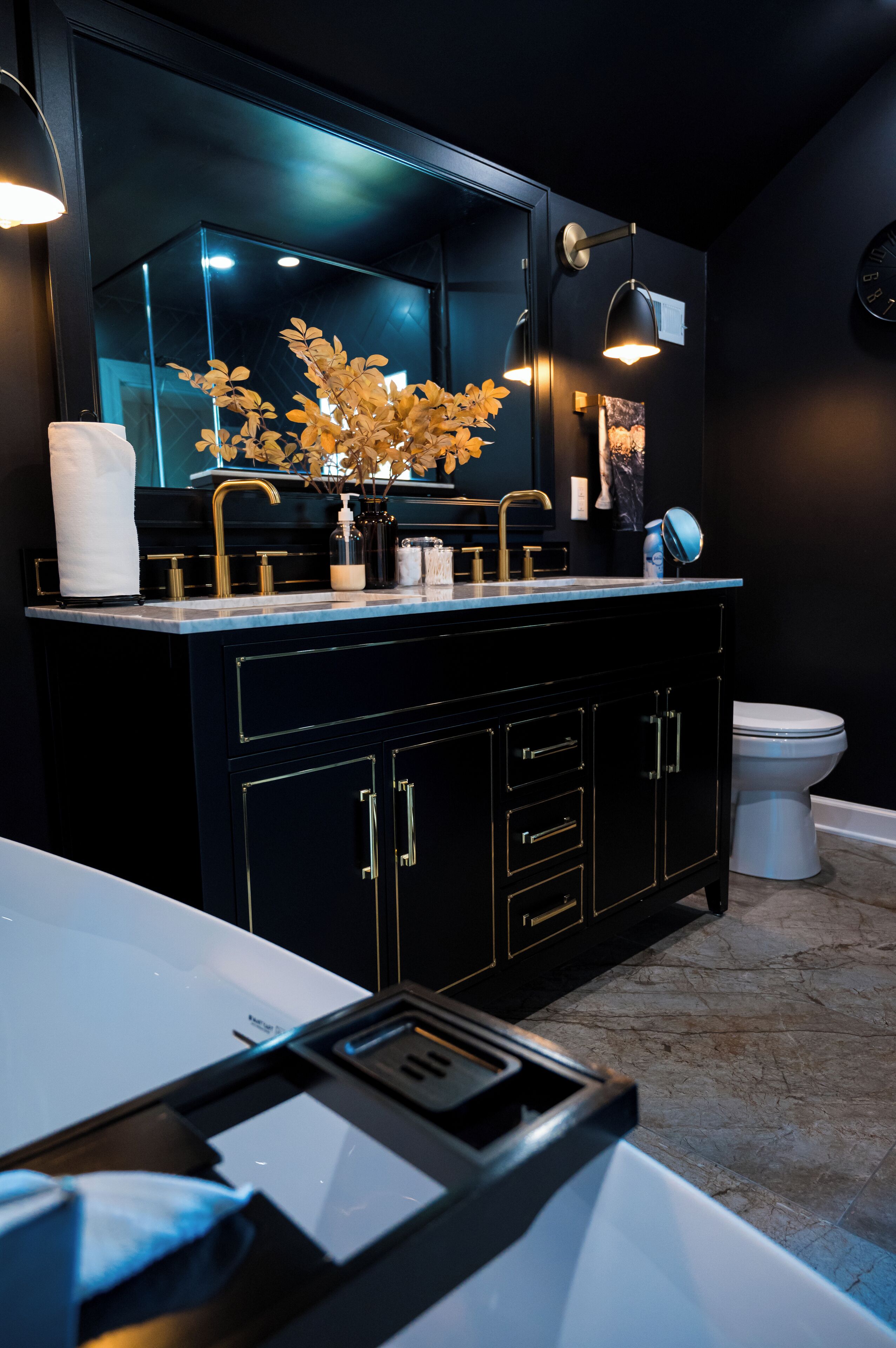 Een moderne badkamer met een zwart wastafelmeubel, gouden details en een grote spiegel.