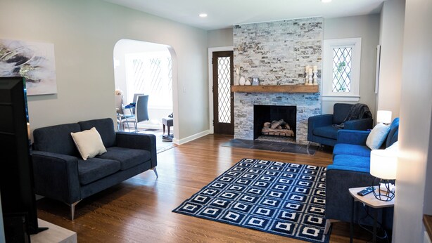 A living room with a fireplace, a blue sofa, a patterned rug, and a television. - Beautifully restored home in Butler Tarkington Walking Distance to Butler Campus (Indianapolis)