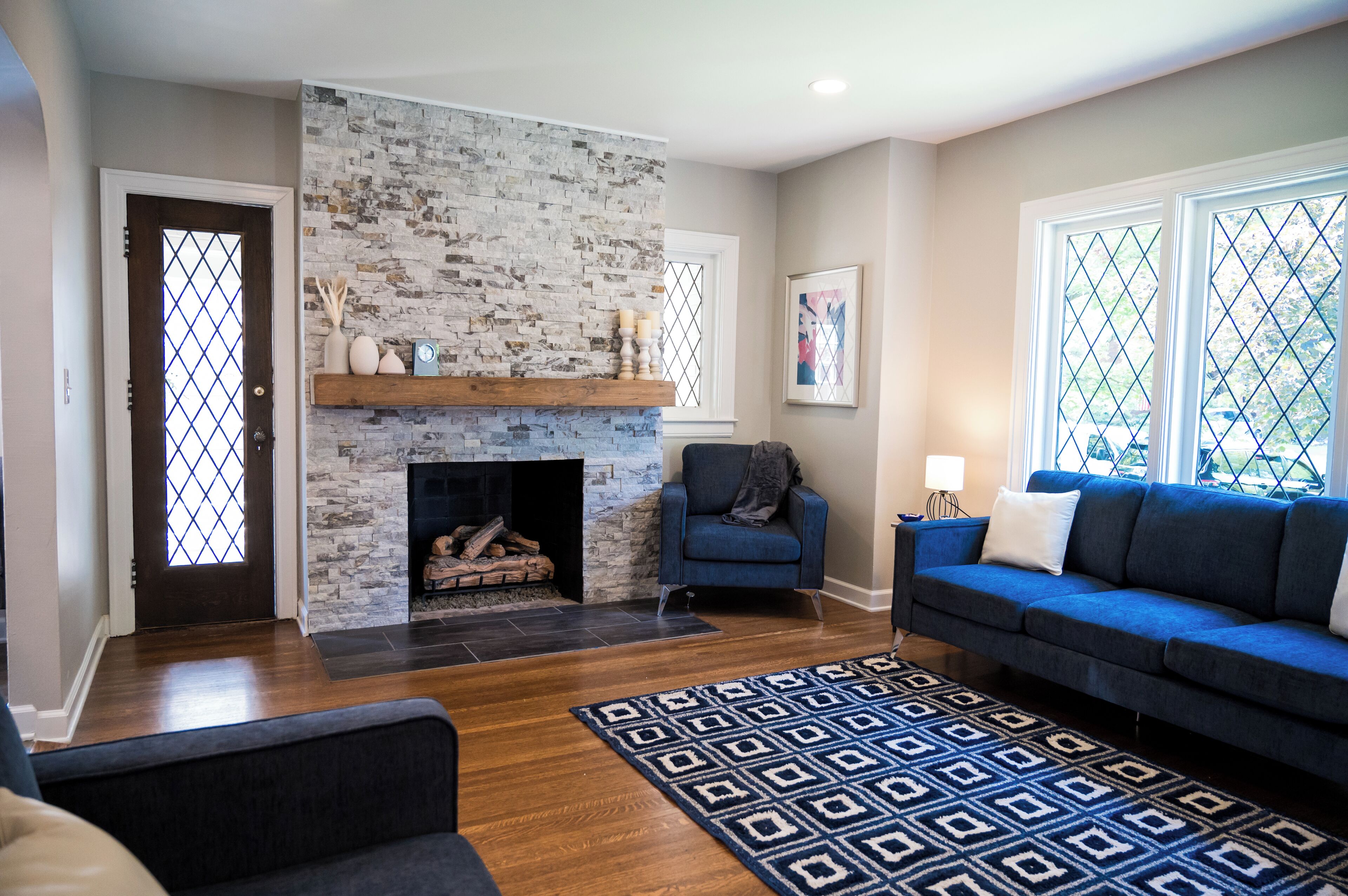 A living room with a fireplace, blue sofa, patterned rug, and a stone accent wall.