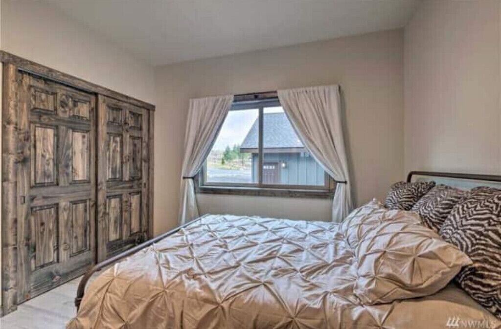 A bedroom with a large bed, a window with curtains, and a wooden wardrobe.