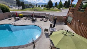 Ein Poolbereich mit Liegestühlen und Sonnenschirmen, Blick auf einen Park mit einem Brunnen, und eine Bergkulisse.