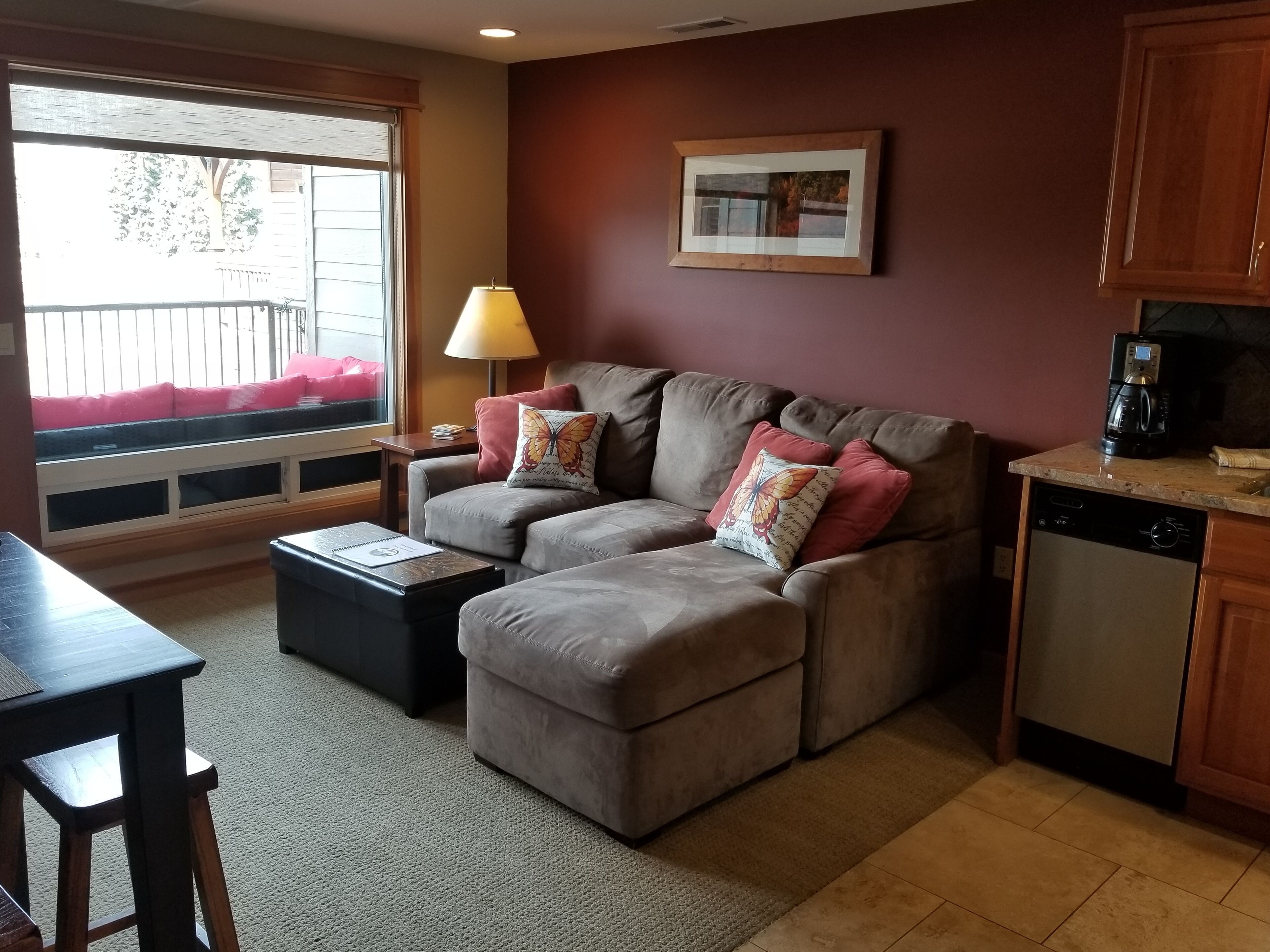 A living room with a sofa, a coffee maker, and a window with blinds.
