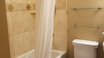 A bathroom with a bathtub, toilet, and glass shelves.