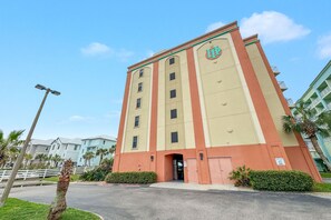 A multi-story hotel with a beige and red facade, a prominent logo on the building, and a gated entrance. - Charming Gulf Front Condo in the Heart of Orange Beach! 2br/2ba with Gulf Views! (Orange Beach)