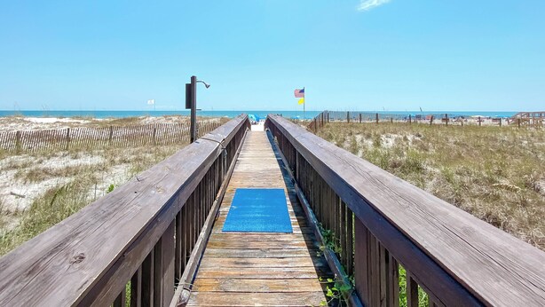 Une promenade en bois mène à une plage où se trouve un tapis bleu au centre.