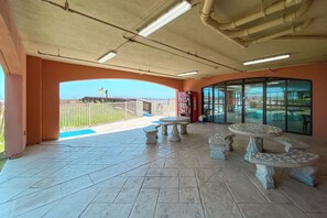 A covered outdoor area with tiled flooring, a pool, and a glass door leading to an indoor space. - Charming Gulf Front Condo in the Heart of Orange Beach! 2br/2ba with Gulf Views! (Orange Beach)