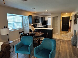 Una cocina moderna con armarios oscuros, una isla central y un comedor con sillas color turquesa.