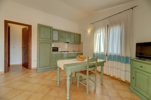 A kitchen with green cabinets, a dining table with a fruit bowl, and a television on a cabinet.