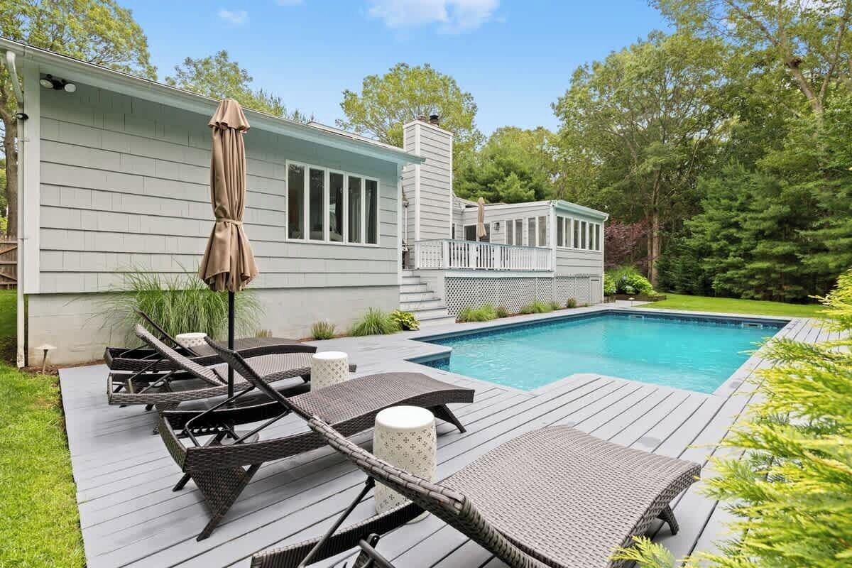 Un espace aménagé au bord de la piscine, avec des chaises longues et un parasol, une petite terrasse et une piscine.