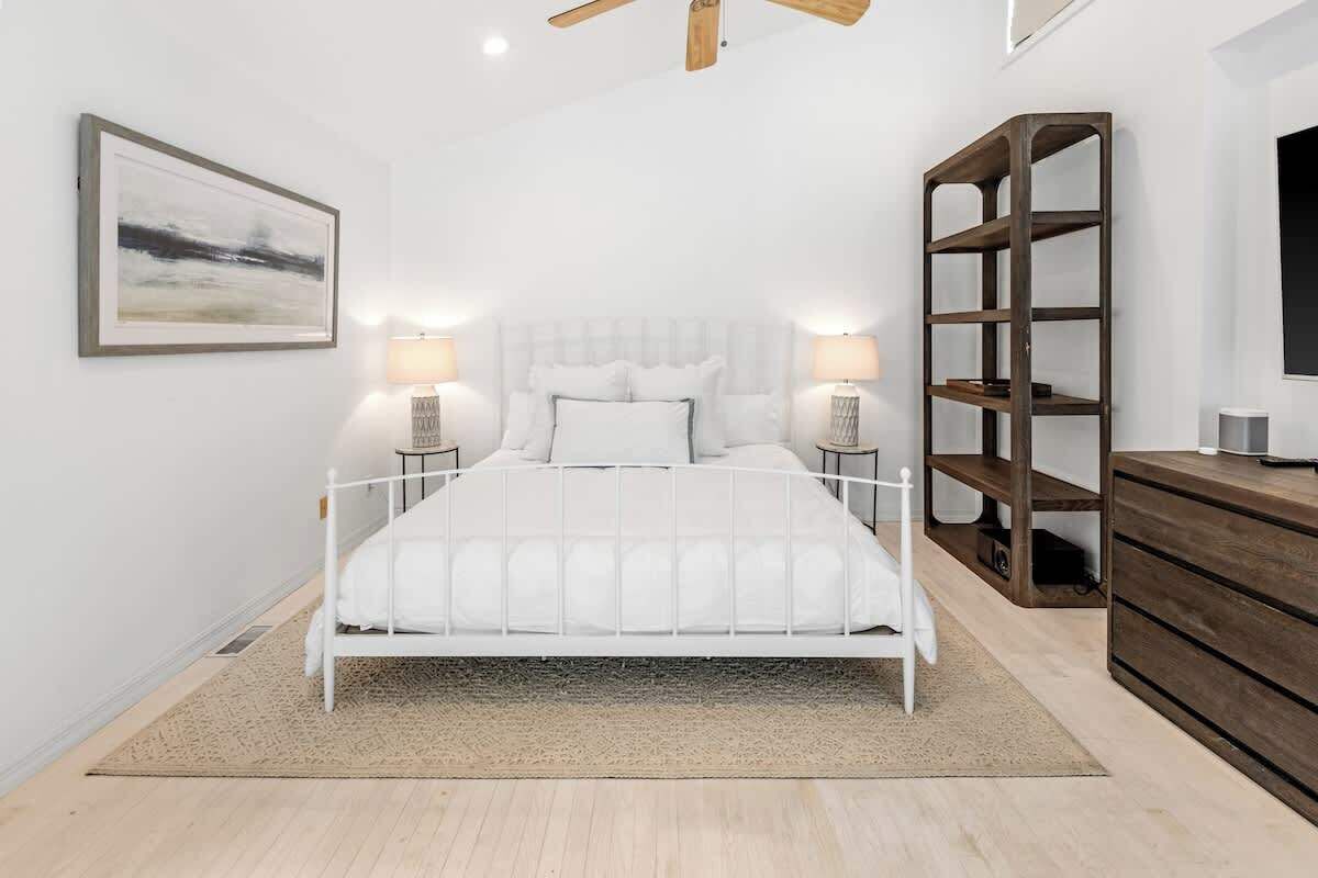 Une chambre à coucher avec un lit blanc, des lampes de chevet, une commode en bois et un tableau encadré au mur.