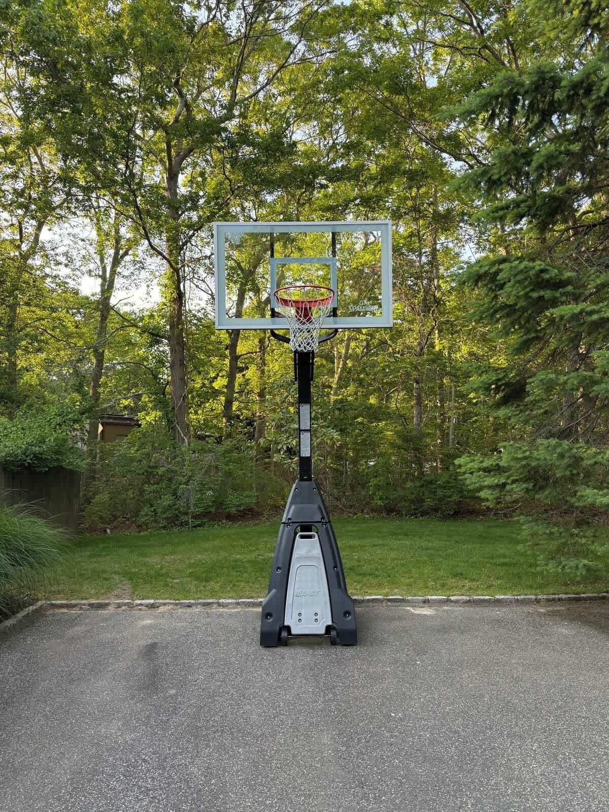 A basketball hoop in a park with a metal frame and a backboard, surrounded by trees and grass.