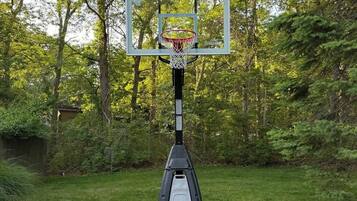 A basketball hoop in a park with a metal frame and a backboard, surrounded by trees and grass.