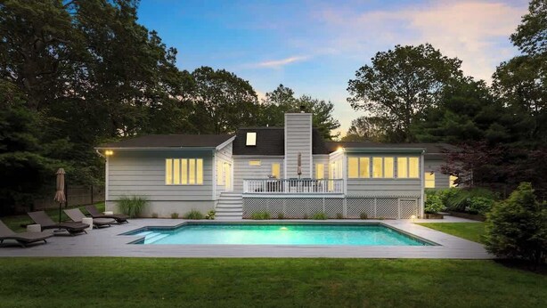 Een modern huis met twee verdiepingen, een zwembad, een overdekt terras en een verzorgd gazon.