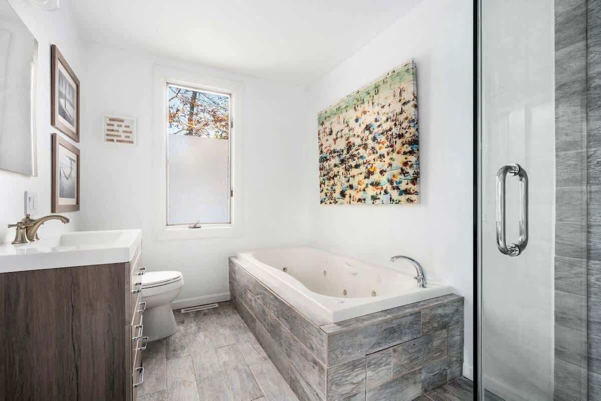 Een moderne badkamer met een vrijstaand bad, een douchecabine met glazen wanden en een groot raam.