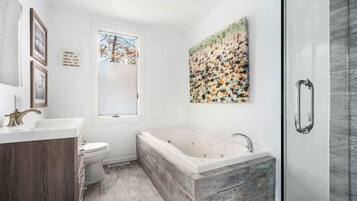 Een moderne badkamer met een vrijstaand bad, een douchecabine met glazen wanden en een groot raam.
