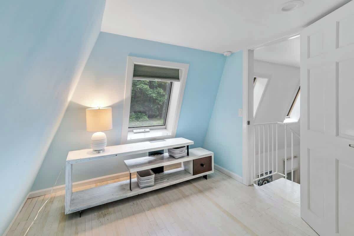 A room with a white console table, a window with blinds, a lamp, and a staircase leading to another level.