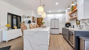 A modern kitchen with a marble island, white cabinetry, and wooden flooring. - Spacious Family Retreat with Pool Gym Sauna Pickleball and Guest Suite SLEEPS 16 (Naples)
