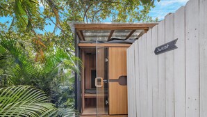 A small, enclosed wooden structure with a glass door, surrounded by lush greenery and a white fence. - Spacious Family Retreat with Pool Gym Sauna Pickleball and Guest Suite SLEEPS 16 (Naples)