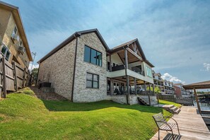 A modern two-story building with a brick facade, large windows, and a covered outdoor area with a wooden deck. - Luxe Waterfront Home in Hot Springs (Hot Springs)