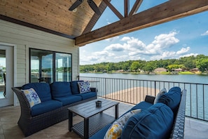 A covered patio with wicker furniture, a table, and a view of a lake and forest. - Luxe Waterfront Home in Hot Springs (Hot Springs)