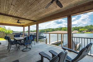 A covered outdoor patio with a table and chairs, a ceiling fan, and a view of a lake and surrounding greenery. - Luxe Waterfront Home in Hot Springs (Hot Springs)