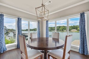 A dining area with a round table, four chairs, and large windows with blue curtains. - Luxe Waterfront Home in Hot Springs (Hot Springs)
