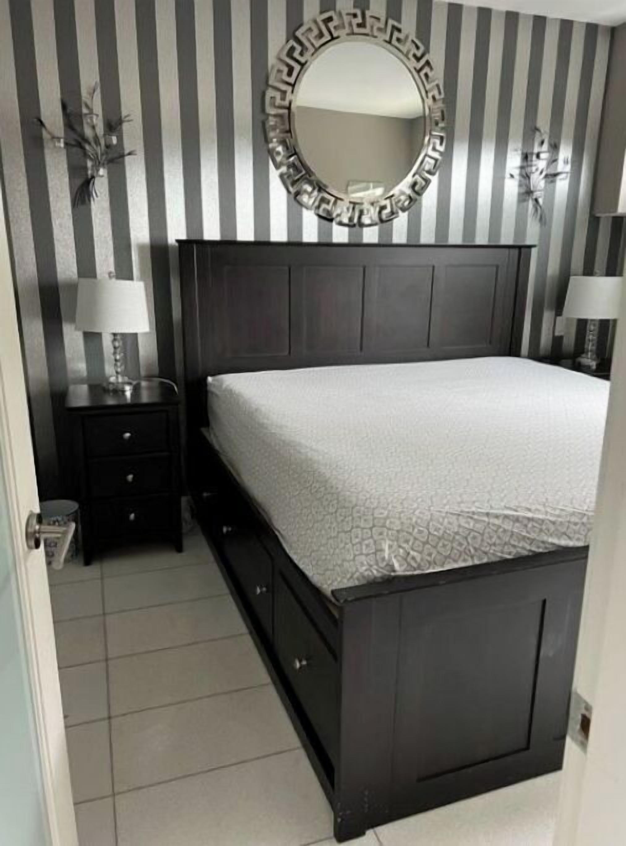 Een slaapkamer met een donker houten bed, een ronde spiegel en behang met strepen.