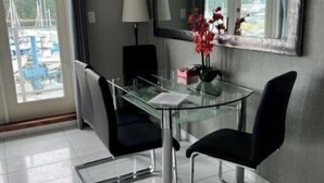 Ett modernt matområde med ett glasbord och svarta stolar, en stor spegel och utsikt över båtar genom en glasdörr.