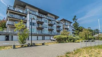 A multi-story residential building with balconies, a parking area, and a landscaped garden.