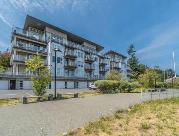 Un immeuble résidentiel à plusieurs étages, doté de balcons, d’un espace de stationnement et d’un jardin aménagé.