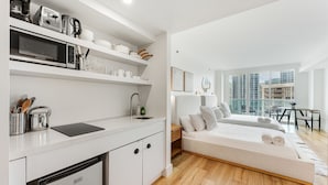 A modern kitchen with white cabinetry, a built-in microwave, and a coffee maker. There is a dining area with a table and chairs, and a large window offering a city view. - ARYA HOTEL STUDIO OCEAN VIEW BALCONY FREE PARKING (Miami)